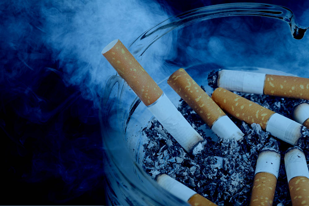 An ash tray full of cigarettes with smoke in the background
